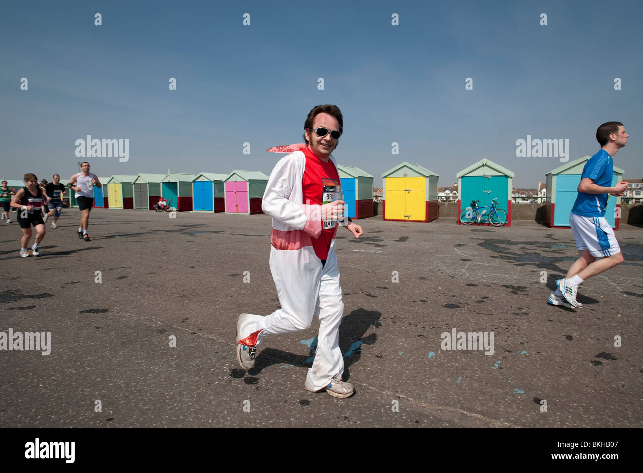 Ein Läufer gekleidet wie ELVIS vorbei Strandhütten auf der Promenade in Hove in den letzten paar Meilen von Brighton Marathon läuft Stockfoto Ein Läufer gekleidet wie ELVIS vorbei Strandhütten auf der Promenade in Hove in den letzten paar Meilen von Brighton Marathon läuft Stockfoto