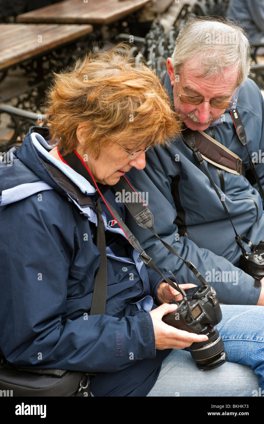 Ein erwachsener Mann mittleren Alters und eine Frau sitzen Prüfung der Rückseite von einem digitalen Objektiv reflex Kamera, beide sind Fotografen. Stockfoto