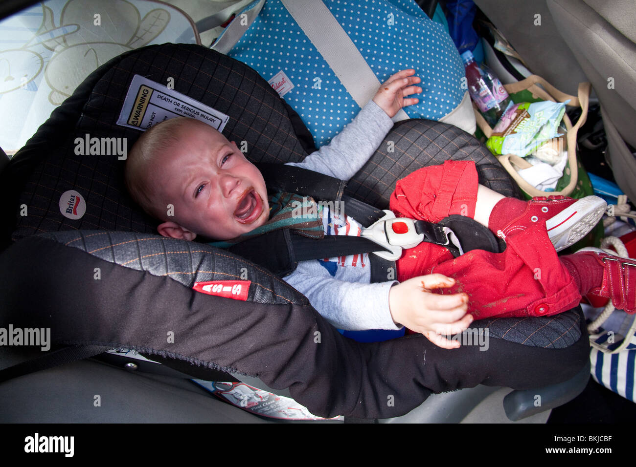 Baby Junge (1 Jahr alt) in einem Autositz für mehr Schokolade mit einem schmutzigen Mund schreien. Stockfoto