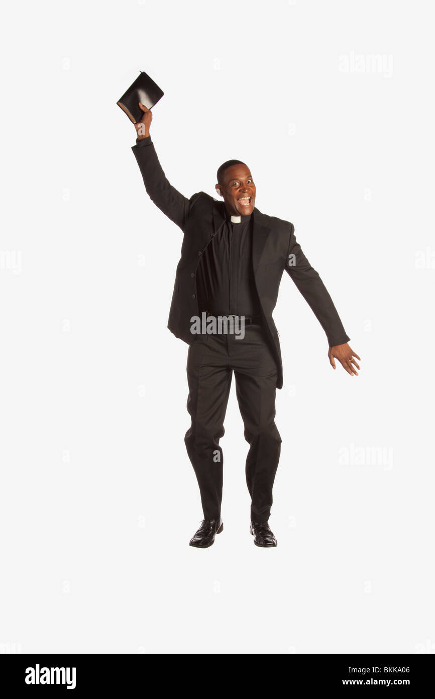 Ein Mann mit einem klerikalen Kragen hält seine Bibel und In die Luft springen Stockfoto