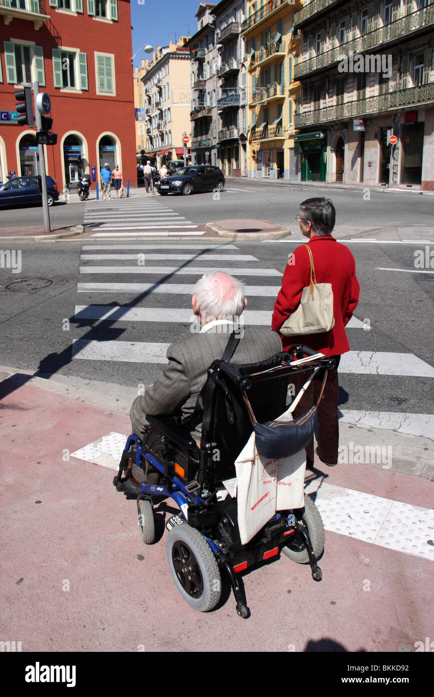 Disabledold Mann sitzt in einem elektrischen Rollstuhl wartet ein Verkehrssignal vor eine Zebrastreifen-Linie, schön, Frankreich Stockfoto