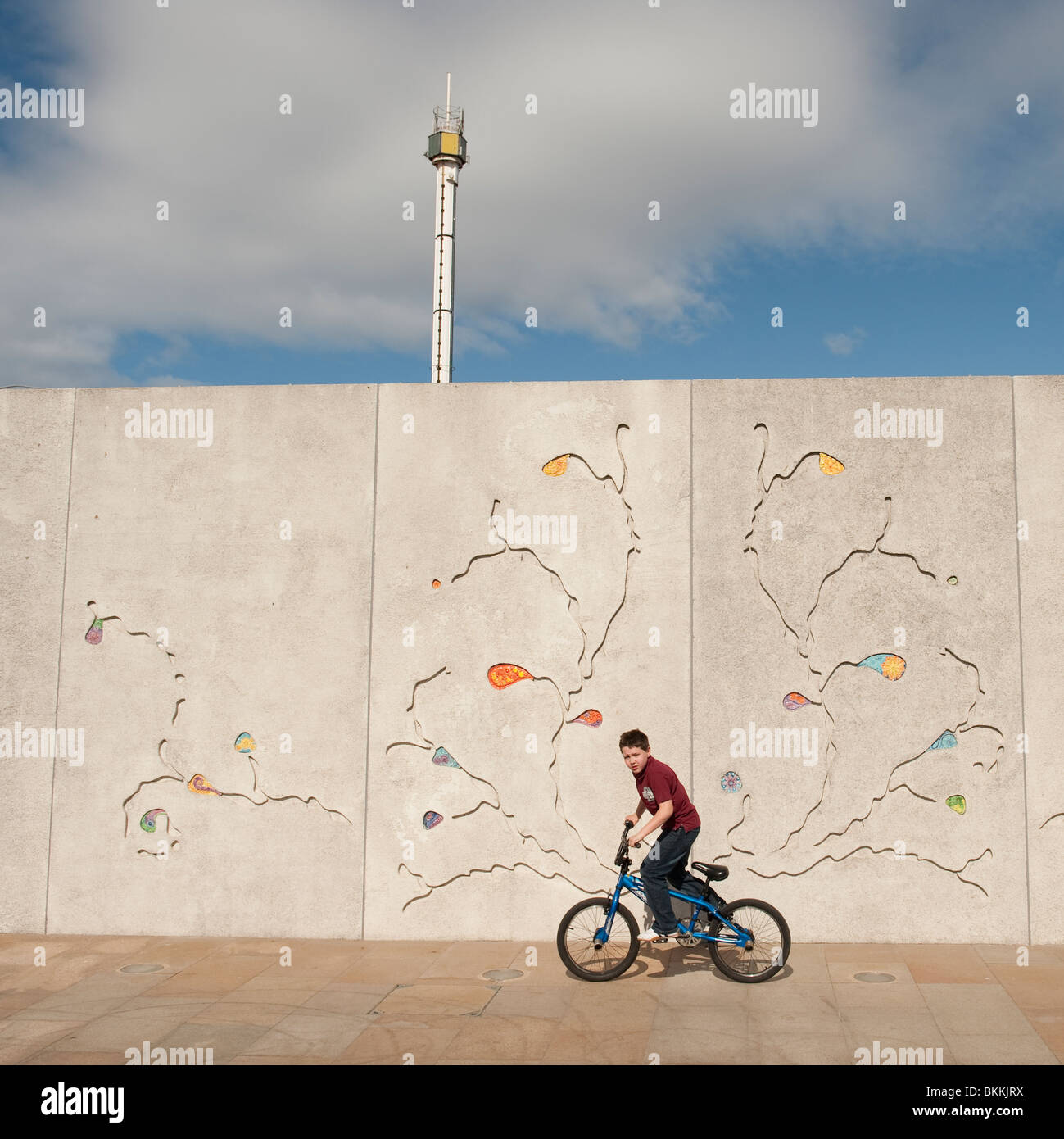 ein Junge auf seinem Fahrrad Radfahren vorbei New Kunst im öffentlichen Raum auf der Promenade und Meer, Rhyl, North wales, UK Stockfoto