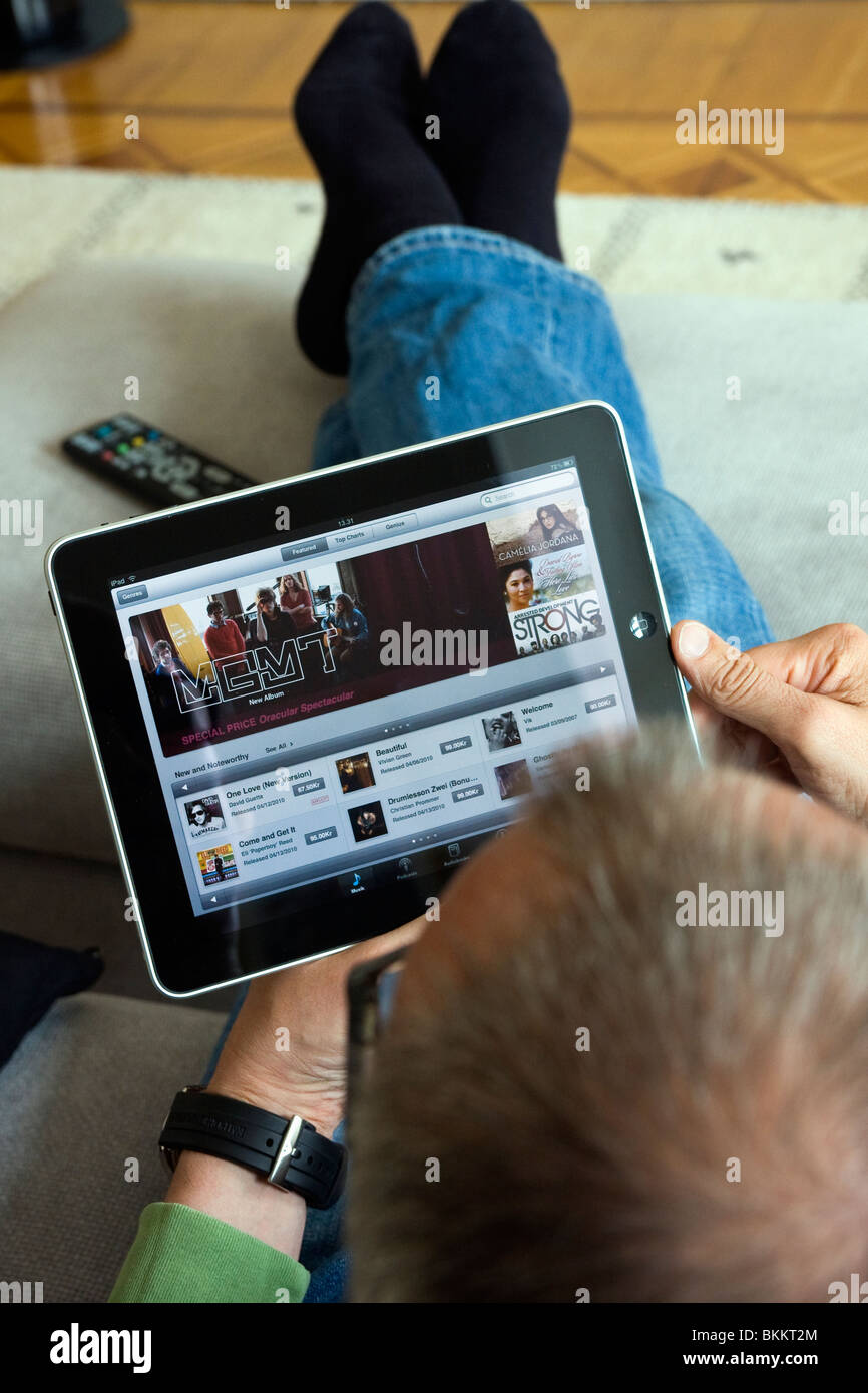 Ein Mann sitzt in seinem Sofa mit einem Apple iPad im iTunes Store für Musik durchsuchen. Stockfoto