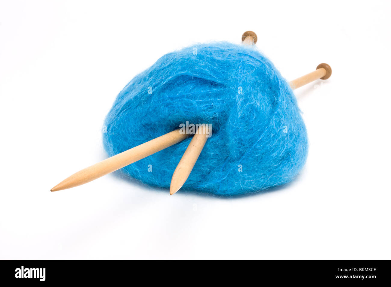 Eine große Kugel aus blaue Mohairwolle durchbohrt mit großen hölzernen Stricknadeln gegen weiß. Stockfoto