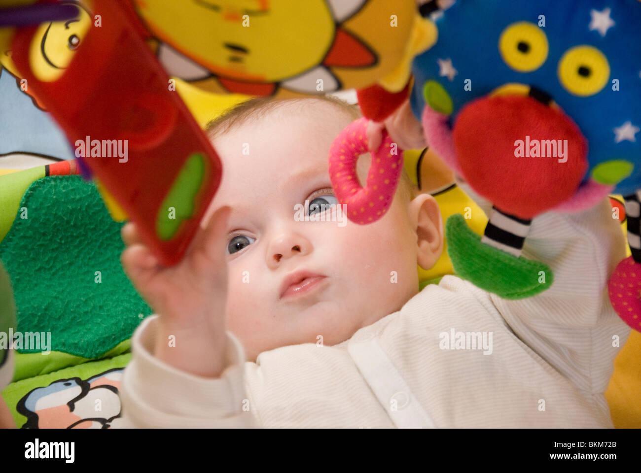 Babymädchen entwickeln Motorsteuerung spielt beim Fang der hängenden Spielzeuge der bunten Babygym Stockfoto