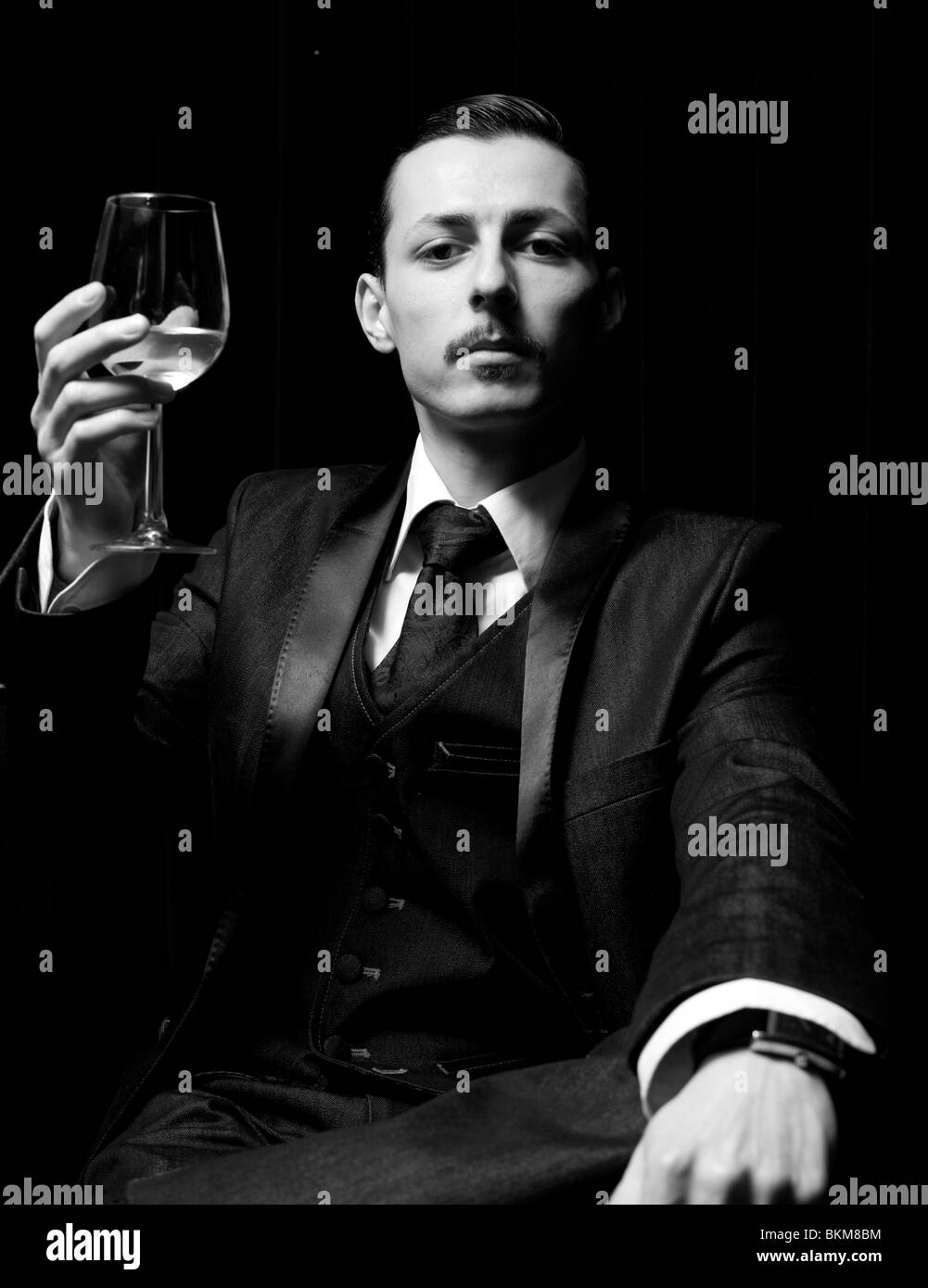 Halblanges Schwarz-Weiß-Porträt eines feierlichen Mannes, der ein Glas Weißwein aufhebt, London, England, Großbritannien. Stockfoto