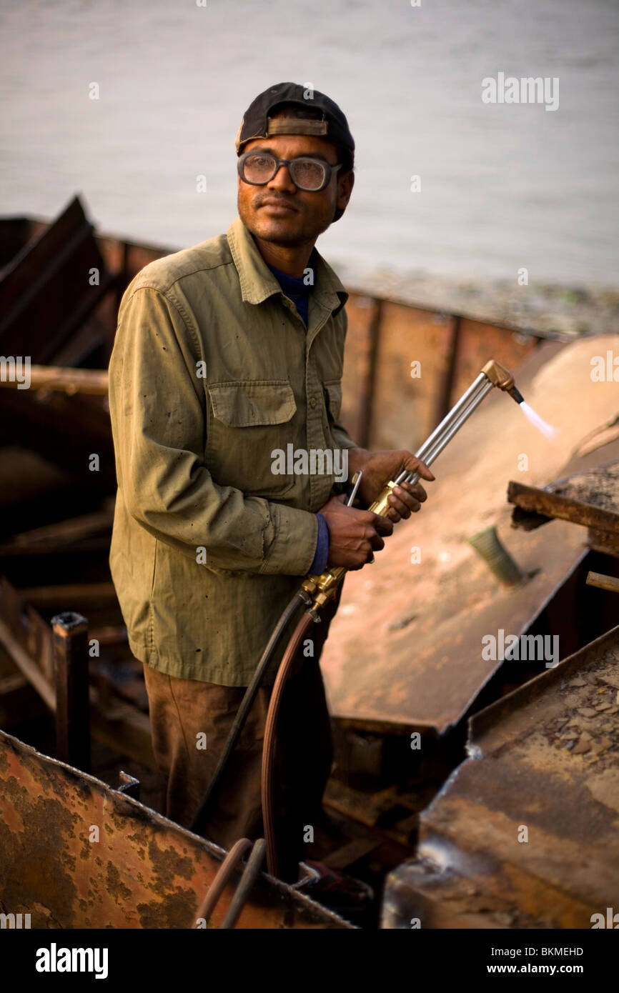 Ein Mann baut ein Boot mit einer Lötlampe und Hammer an den Ufern des Flusses Karnaphuli unter der Kalurghat-Brücke, Chittago Stockfoto