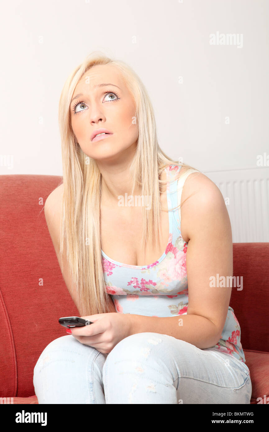 Blonde Frau sitzt auf einem roten Sofa sucht eine Telefon halten. Stockfoto