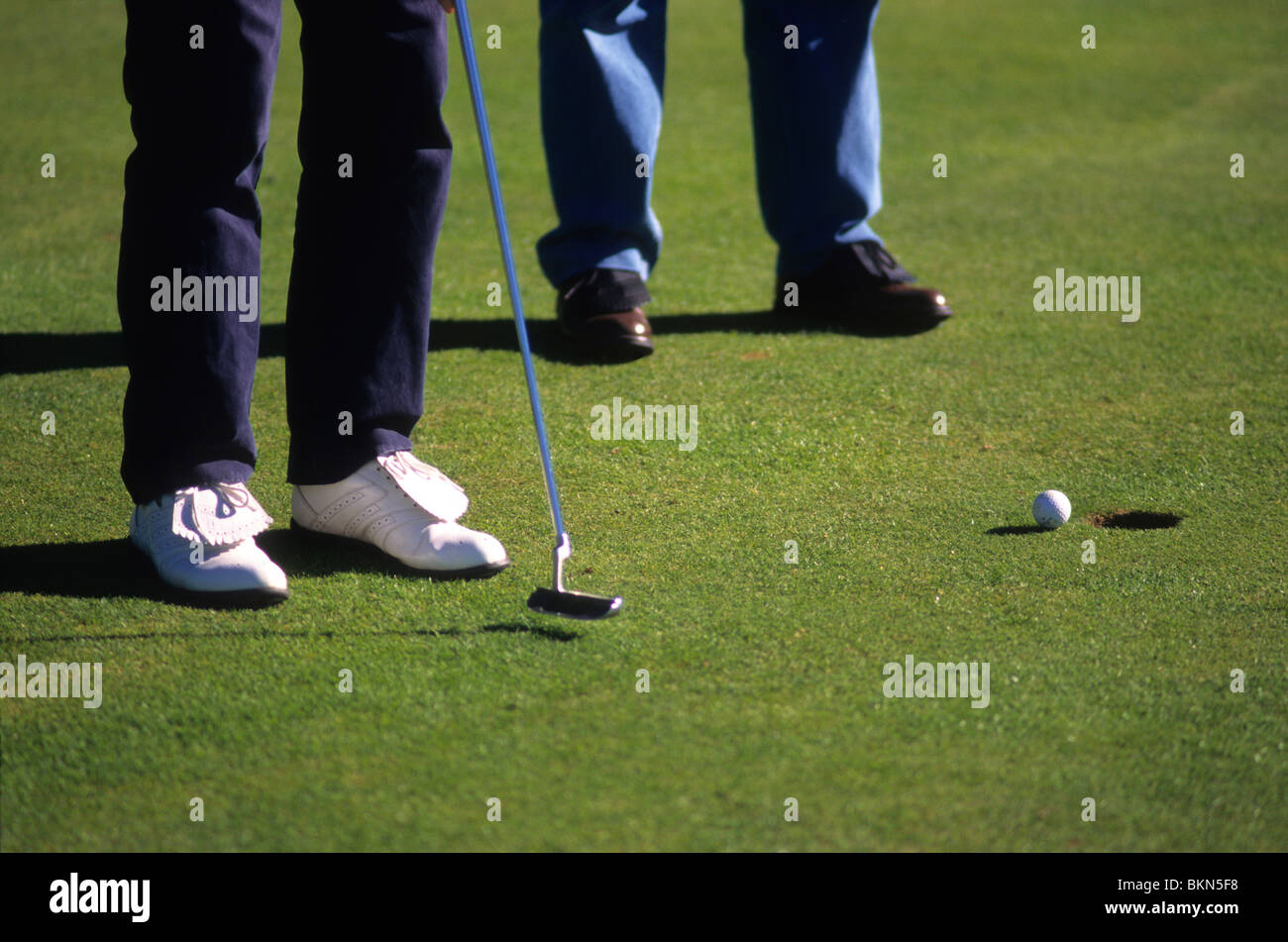 Zwei Golfer setzen Golfball ins Loch auf einem Golfplatz. Stockfoto