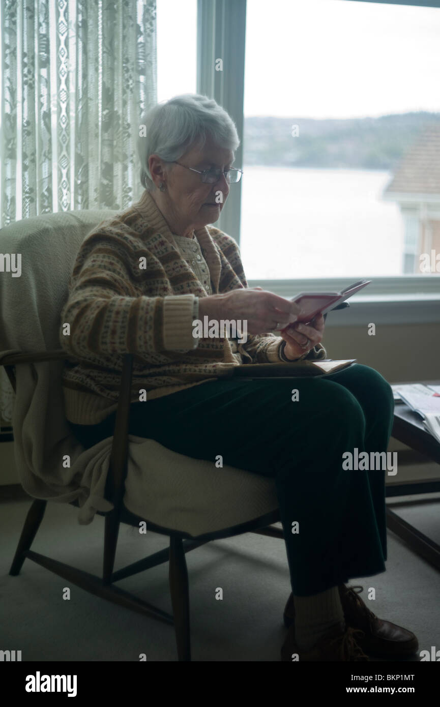 Alte Frau sitzt im Stuhl von Fenster und kleines Fotoalbum blättert. Stockfoto