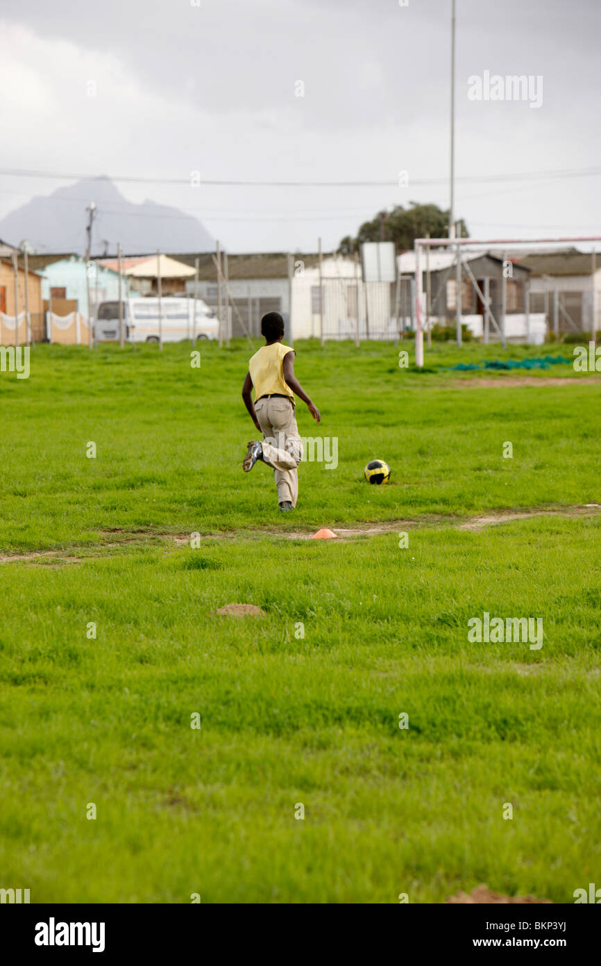 Junge treten Fußball im Township Stockfoto