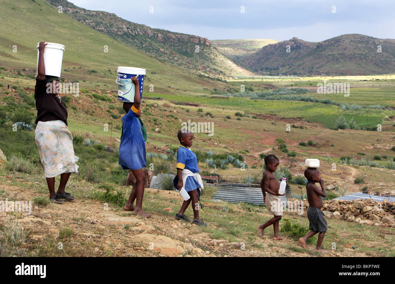 Lesotho: Familie Wasser aus einem Brunnen im Eimer auf dem Kopf tragen Stockfoto