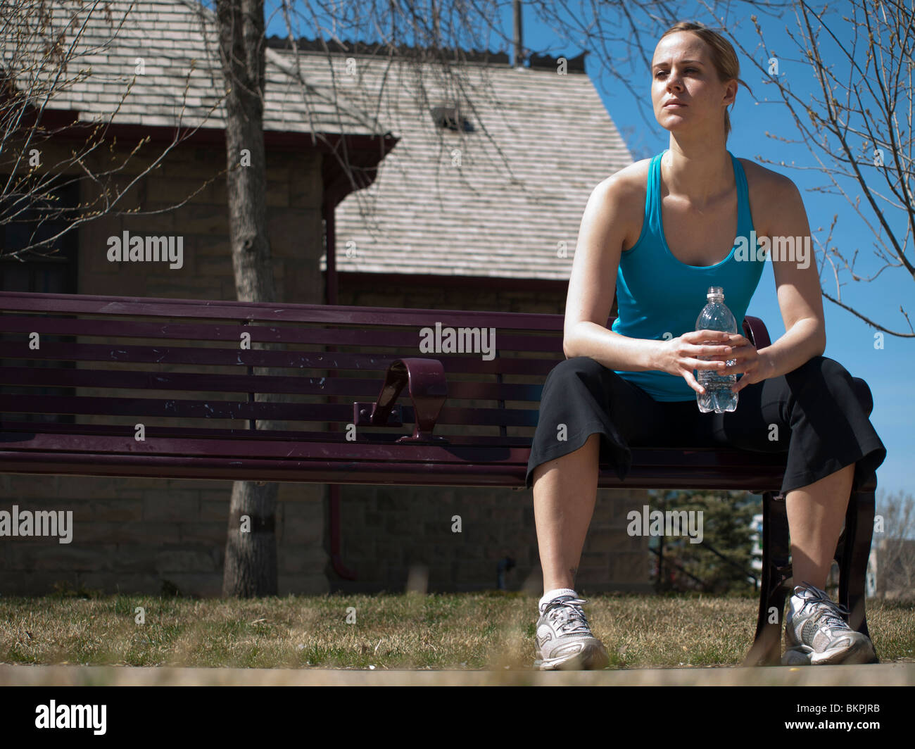 junge Frau sitzt auf der Bank mit Wasserflasche Stockfoto