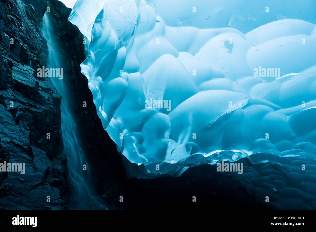 Ein Wasserfall rieselt seinen Weg nach unten die Felswand der eine Eishöhle im Inneren der Mendenhall-Gletscher, Juneau, Alaska Stockfoto