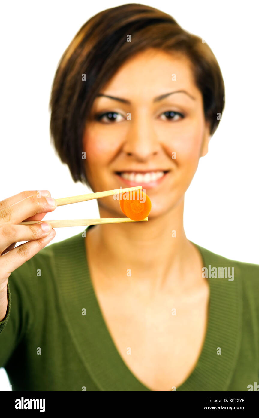Lächelnde Frau hält ein Stück gekochte Karotten mit Stäbchen vor den Mund. Stockfoto