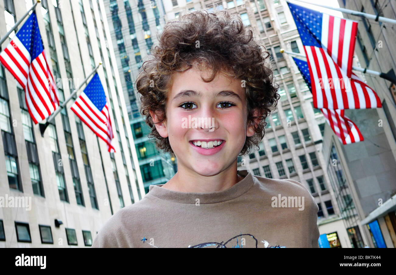 Junge lächelnd mit amerikanischen Flaggen und Gebäude im Hintergrund. Stockfoto