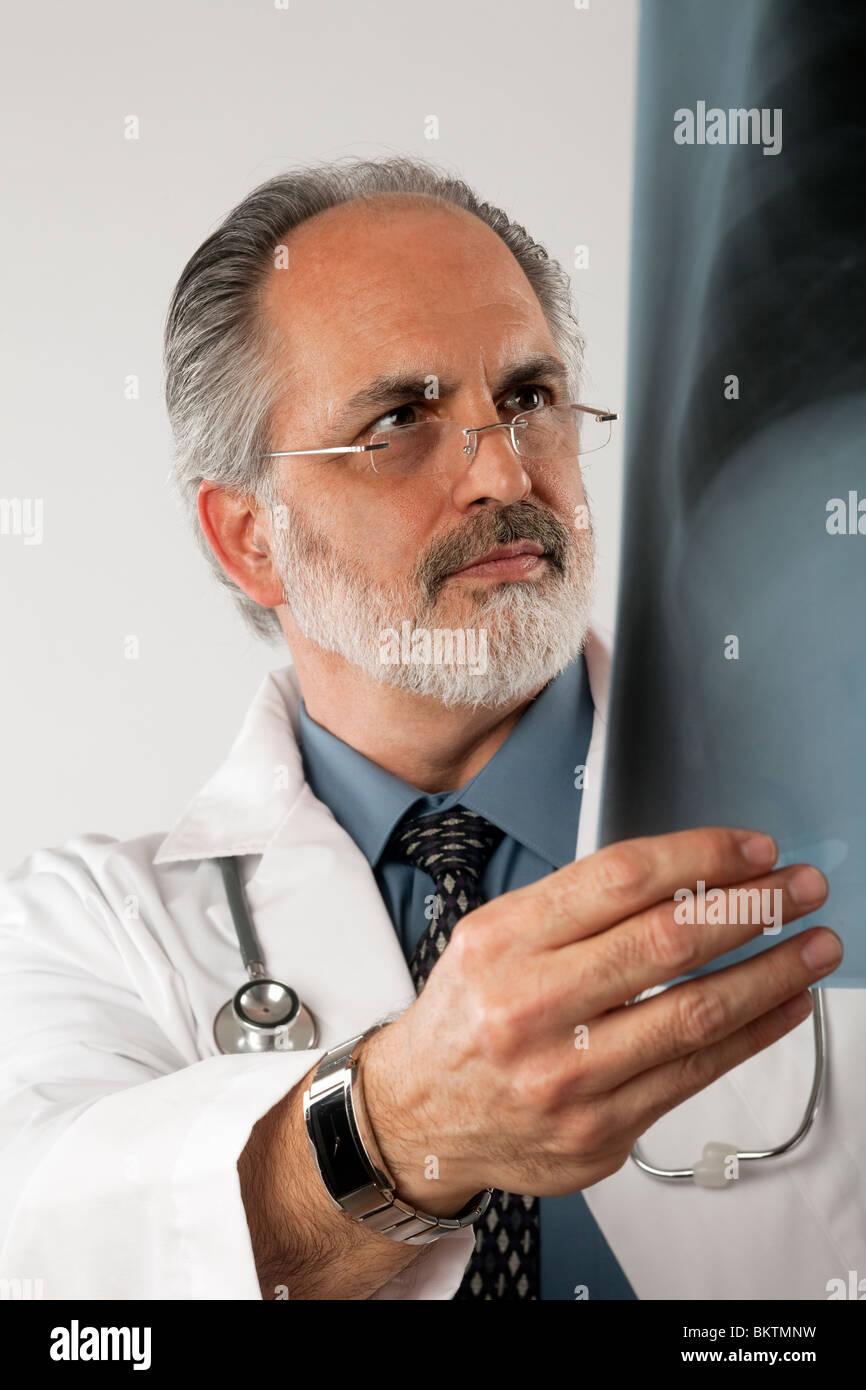 Porträt eines Arztes tragen Brillen und einen weißen Laborkittel und eine Röntgenaufnahme aufmerksam betrachten. Vertikale erschossen. Isoliert auf weiss. Stockfoto