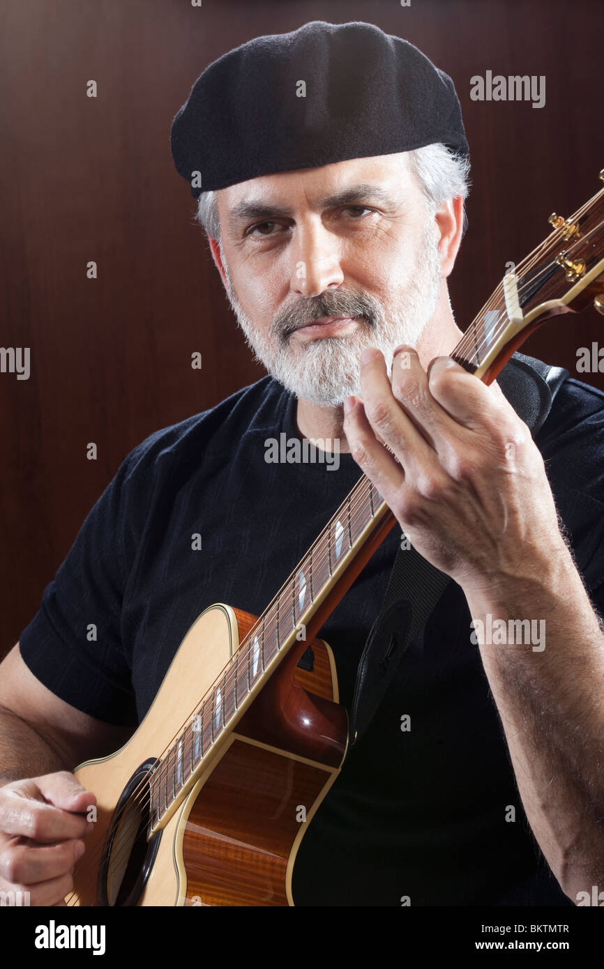 Porträt von einem Mann mittleren Alters, eine schwarze Mütze und T-shirt und eine akustische Gitarre zu spielen. Er schaut in die Kamera Stockfoto