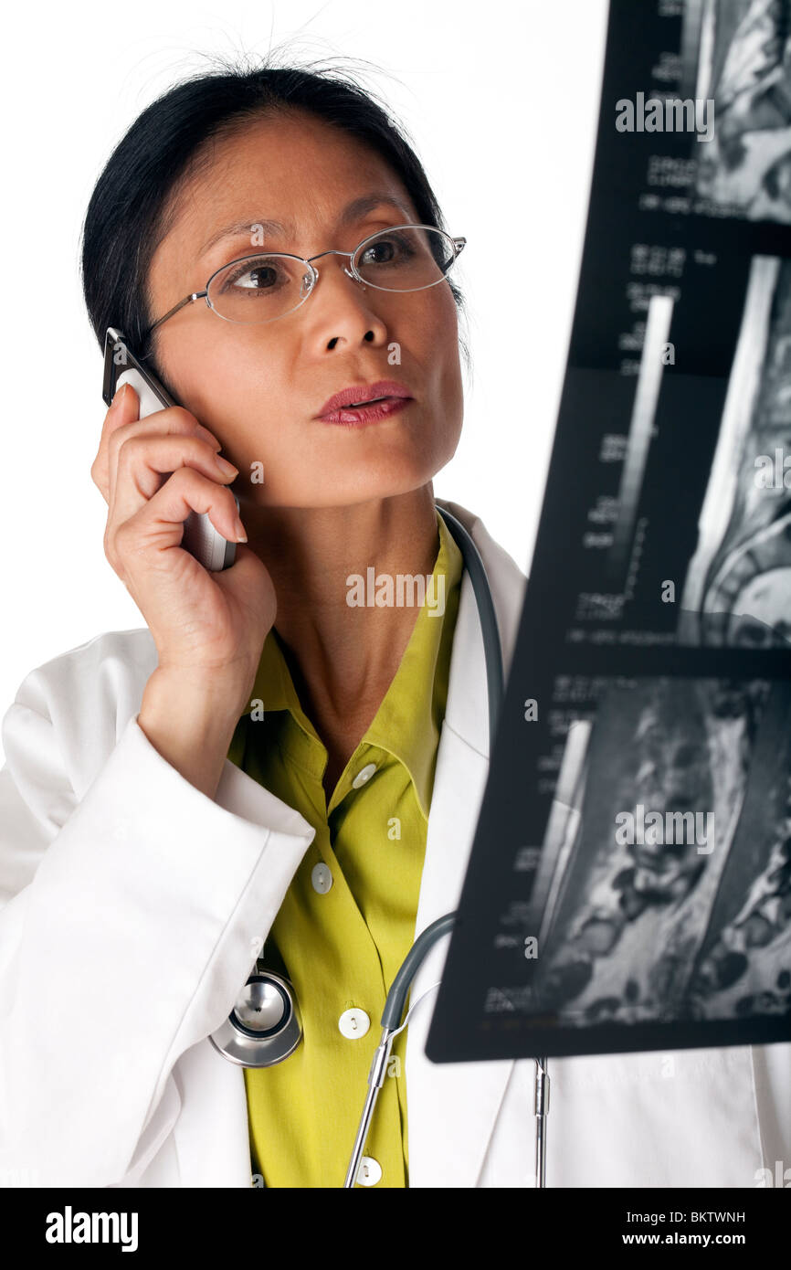 Asiatische Ärztin eine MRT-Untersuchung während des Gesprächs auf ein Handy zu betrachten. Vertikale erschossen. Isoliert auf weiss. Stockfoto