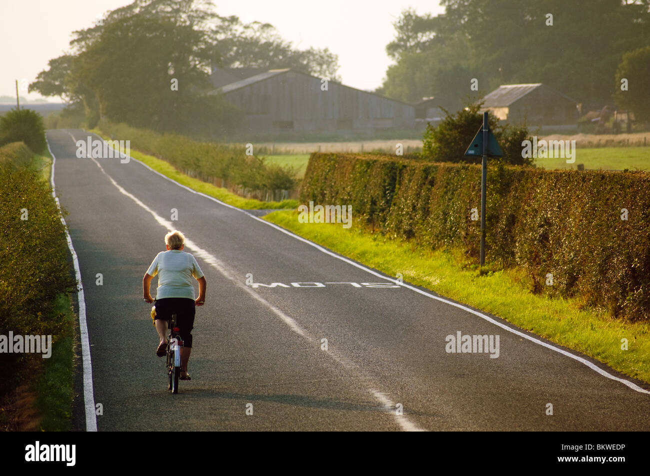 Woman cycling on empty road on the plain of the Fylde, Lancashire, England Stockfoto