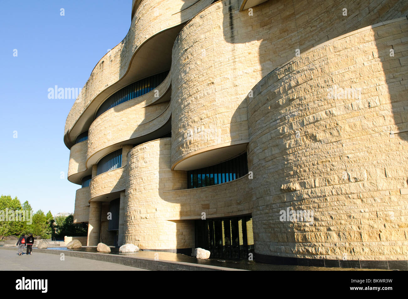 National Museum of the American Indian Exterior Washington DC // WASHINGTON DC – Außenansicht des National Museum of the American Indian der Smithsonian Institution. Das Gebäude hat ein markantes kurvenförmiges Design, das aus Kasota-Kalkstein gebaut wurde, und ist von einer Landschaft umgeben, die Wasserspiele und große Felsbrocken umfasst. Stockfoto