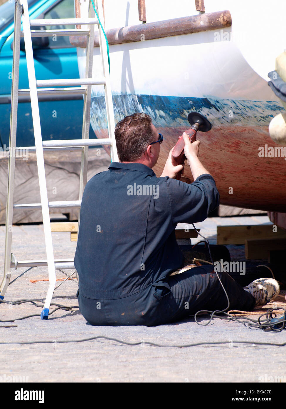 Mann, Abschleifen Malerarbeiten auf Boot, Cornwall, UK Stockfoto