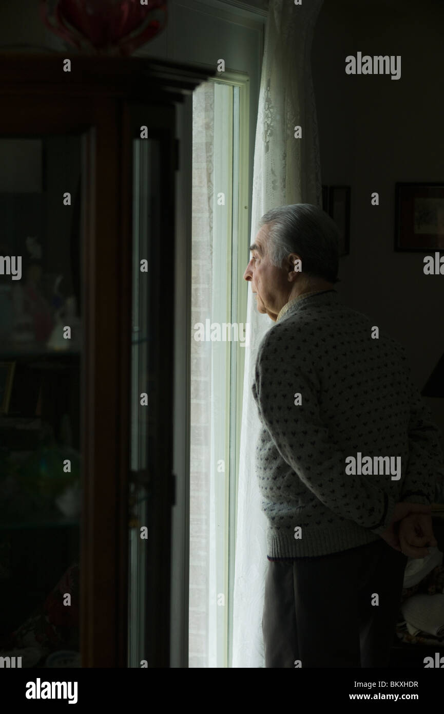Alter Mann steht mit Hände hinter Rücken, aus Full-length Fenster zu schauen. Stockfoto