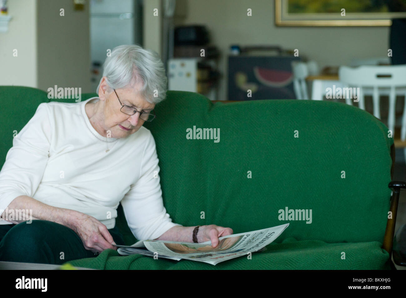 Alte Frau sitzt auf Chesterfield lesen Zeitung Stockfoto