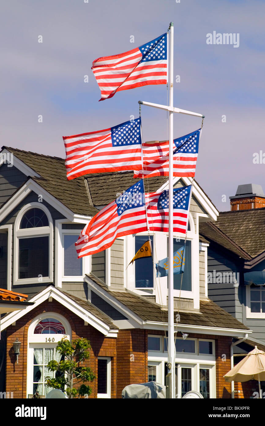 Fünf rote Fahnen weißen und blauen US-Welle in der Brise aus einem Fahnenmast vor einem Haus auf Balboa Island in Newport Beach, Kalifornien, USA. Stockfoto