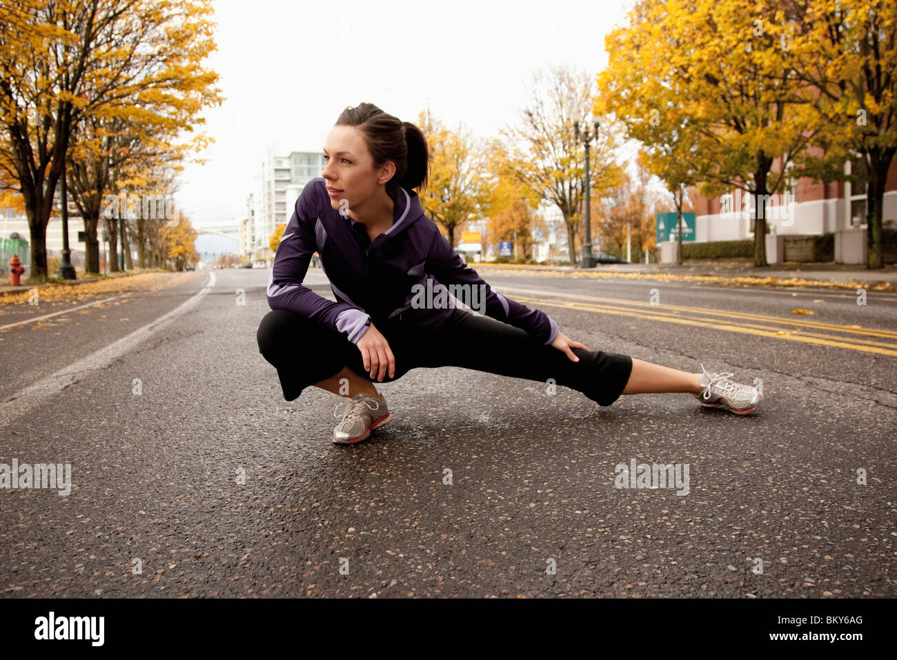 Eine sportliche Frau in eine lila Jacke erstreckt sich entlang einer verlassenen Straße in Portland, Oregon. Stockfoto
