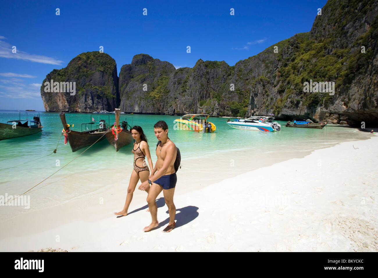 Ein junges Paar zu Fuß über den Strand, verankerte Schiffe im Hintergrund, Maya Bay, eine wunderschöne malerische Lagune, berühmt für die Hollywo Stockfoto