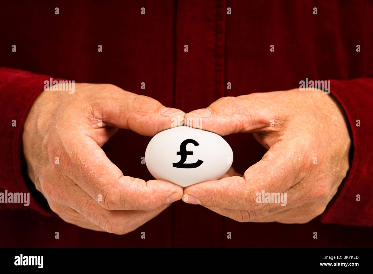 Mann hält weißes Ei mit einem Nummernzeichen (£) geschrieben steht, als Symbol für die Zerbrechlichkeit von Geldangelegenheiten; die sprichwörtliche "Notgroschen". Stockfoto
