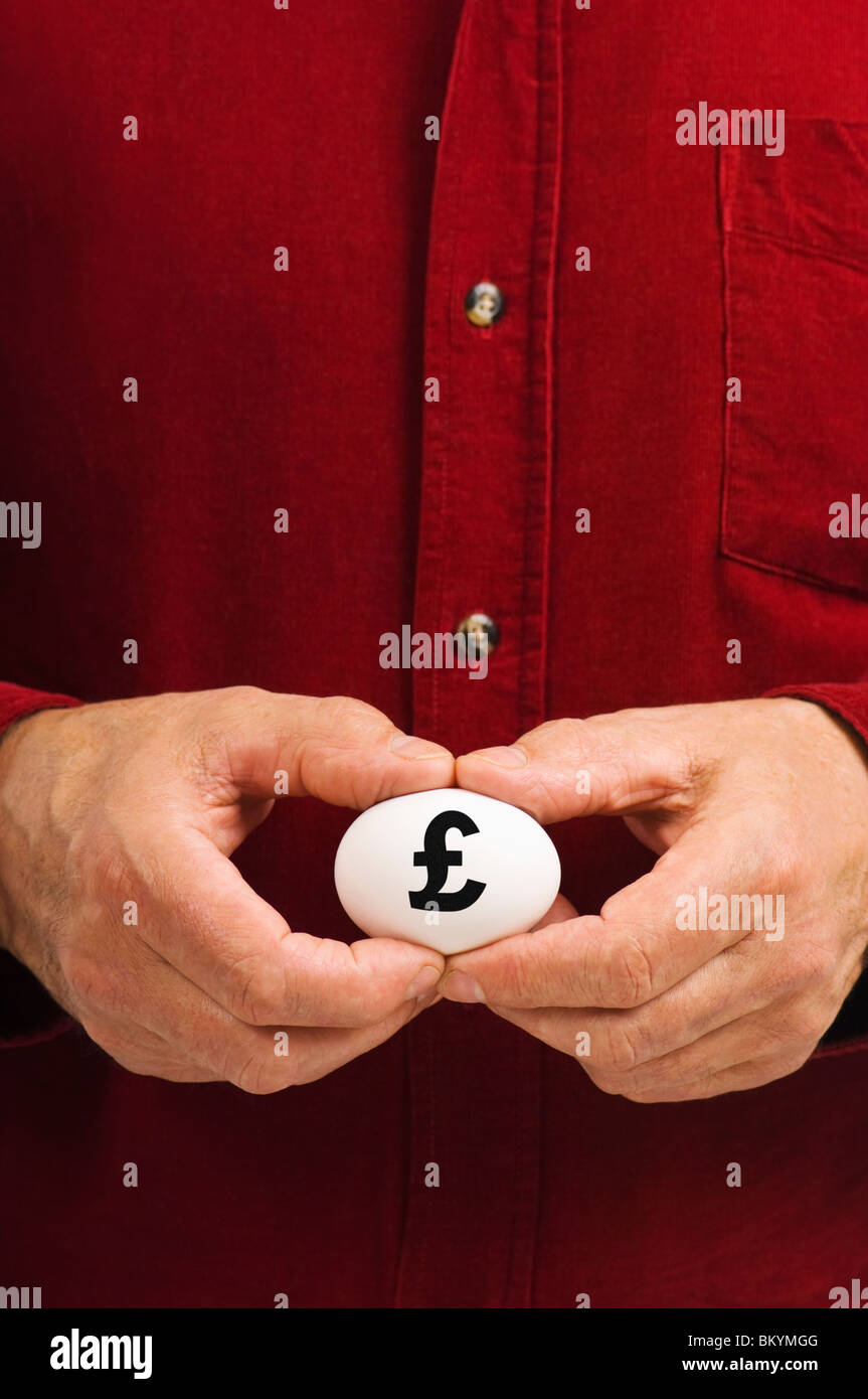 Mann hält weißes Ei mit einem Nummernzeichen (£) geschrieben steht, als Symbol für die Zerbrechlichkeit von Geldangelegenheiten; die sprichwörtliche "Notgroschen". Stockfoto