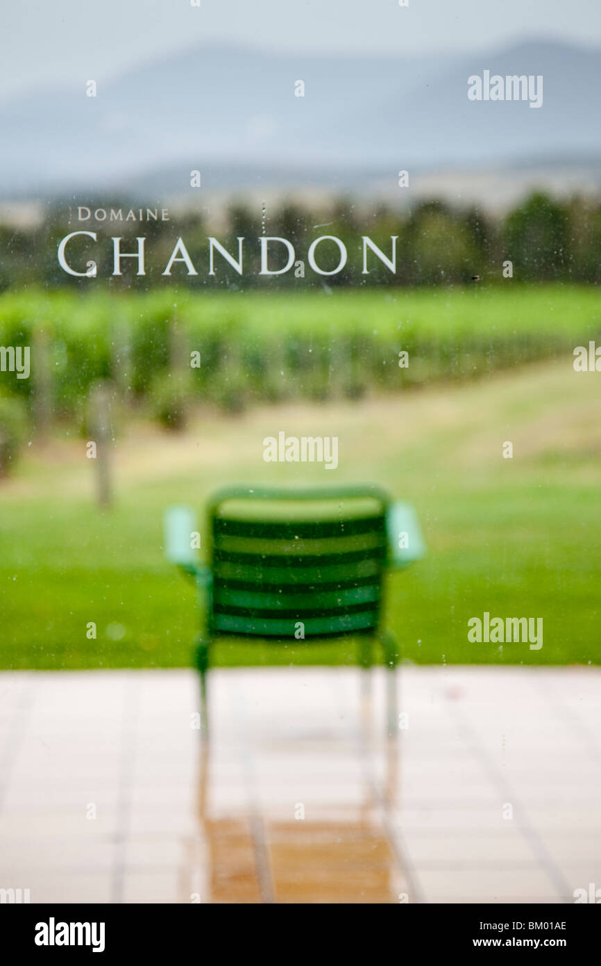 Weingut Domaine Chandon mit einem grünen Stuhl auf einem regnerischen Patio mit Blick auf den Weinberg, Reben, Büschen, Bäumen und Hügeln. Stockfoto