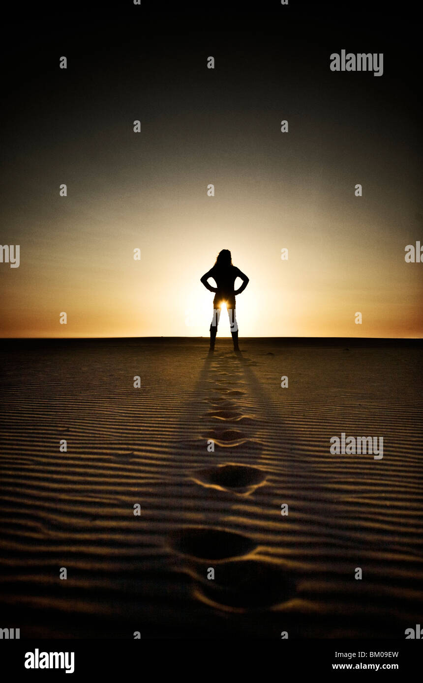 Junge Frau im Abstand stehen am Strand bei Sonnenuntergang mit Fuß druckt in sand Stockfoto