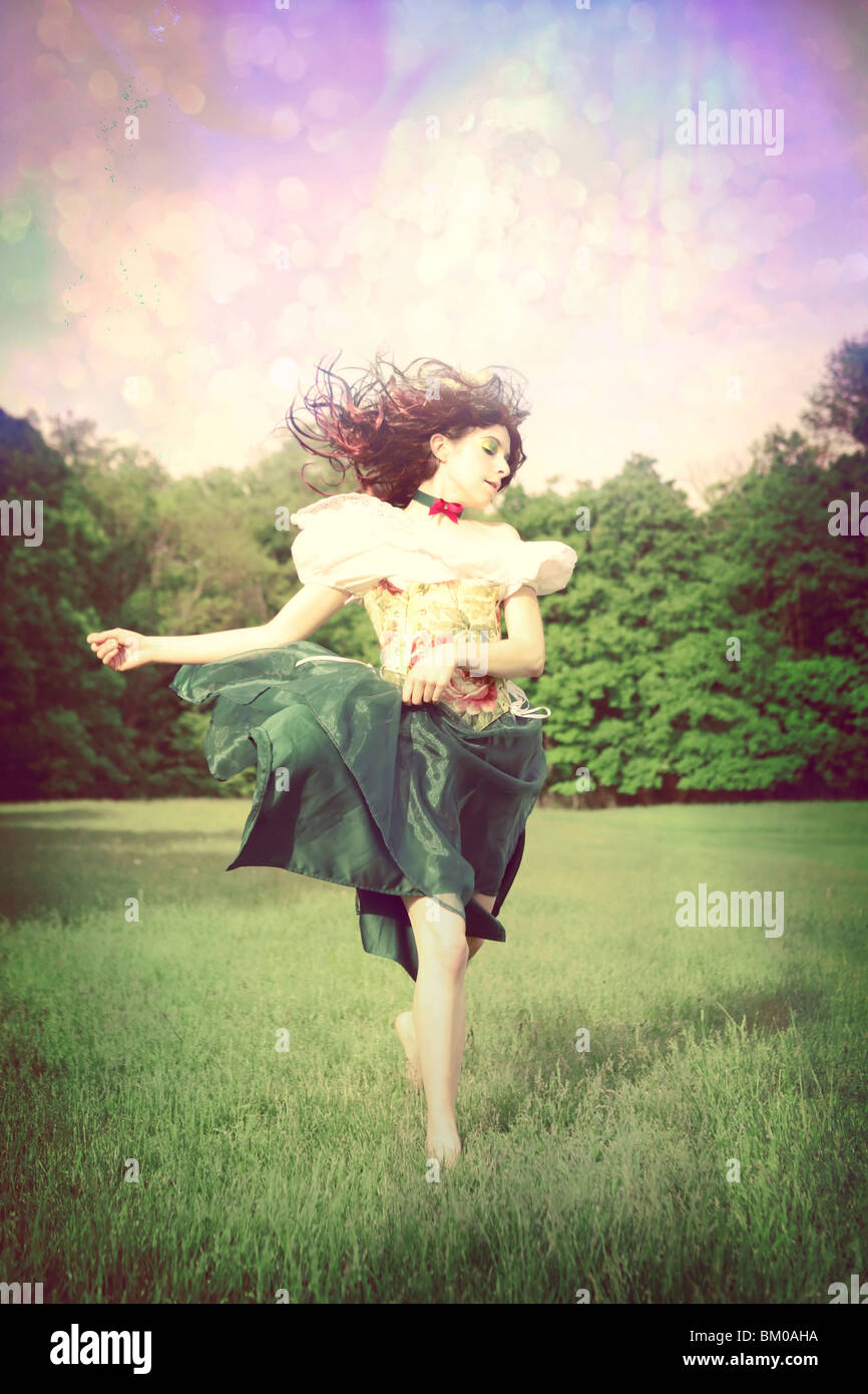 Tänzelnde Mädchen in einem Feld mit vom Wind verwehten Haaren und einem geblümten Kleid Stockfoto