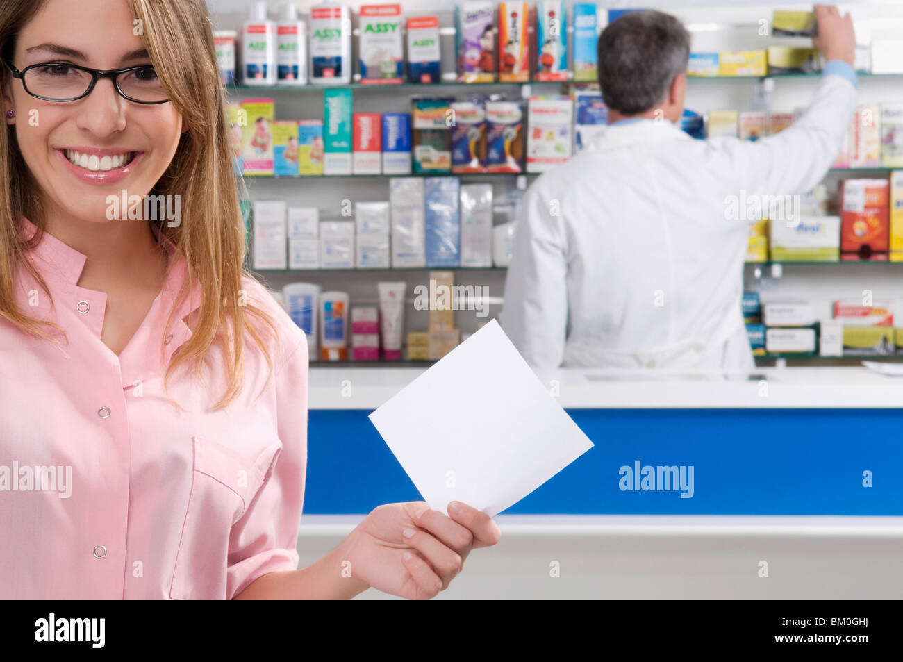 Apothekerin hält ein Rezept und einen männlichen Apotheker im Hintergrund Stockfoto