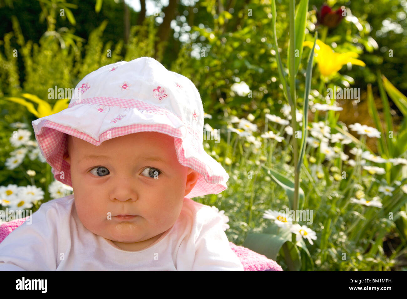 Schöne 6 Monate alten weiblichen Mädchen Säugling Baby Kleinkind in rosa Sonnenhut Hut in Sonne Sonnenschein im Garten draußen im Freien mit blau Stockfoto