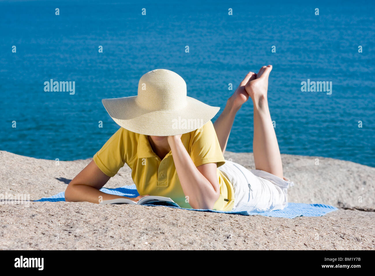 Womand auf einem Felsen am Meer liegend ein Buch lesen Stockfoto