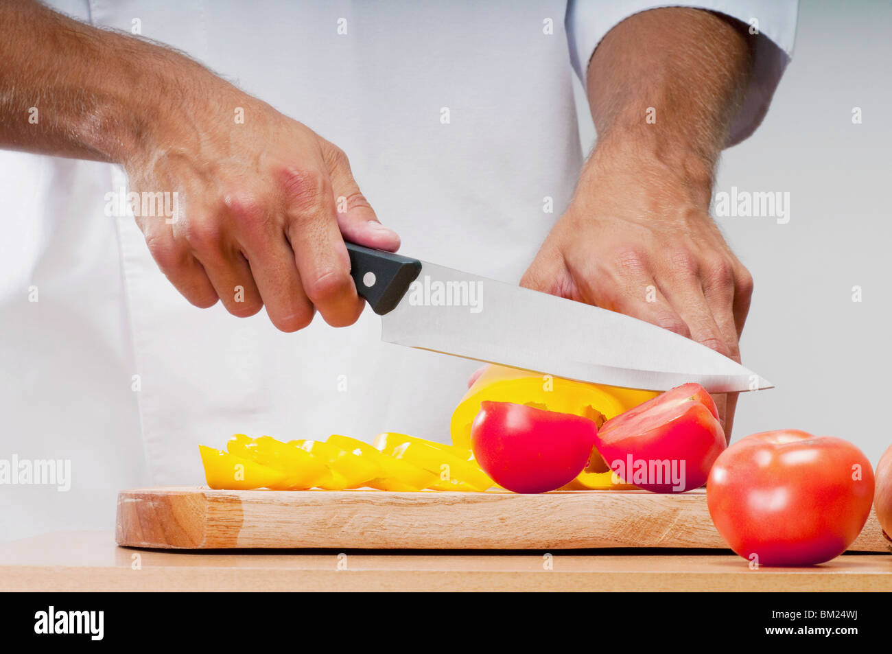 Man schneidet eine gelbe Paprika und Tomaten Stockfoto