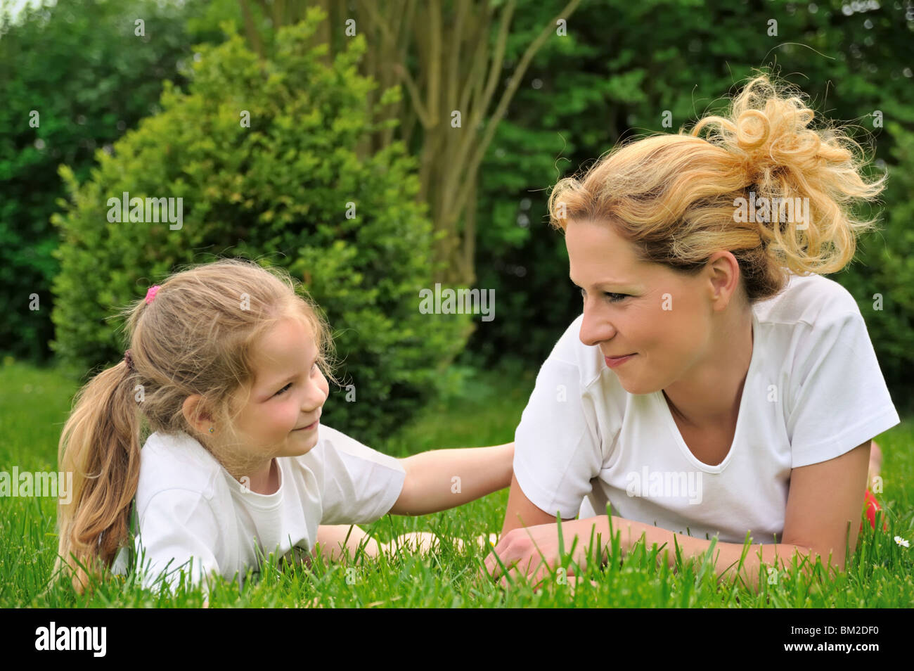 Junge Mutter und Tochter, die Verlegung auf dem Rasen Stockfoto