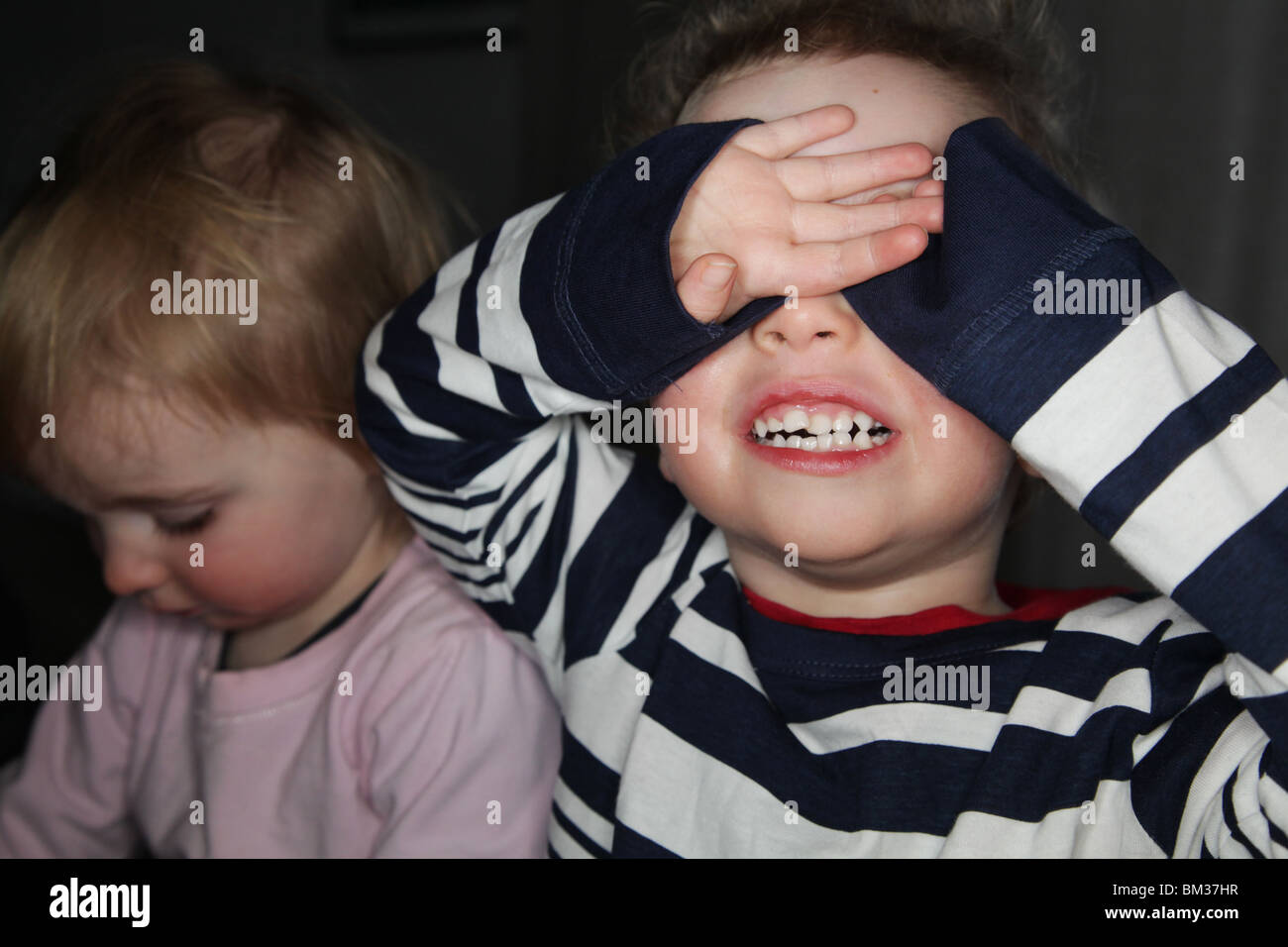 PEEK-A BOO: Ein zweijähriger Junge versteckt sich und sucht einen Blick ein Buh-GUCK-Guck-Guck-Guck-Guck-Versteck-Gesicht-Modell, aufgenommen mit Ringblitz Stockfoto