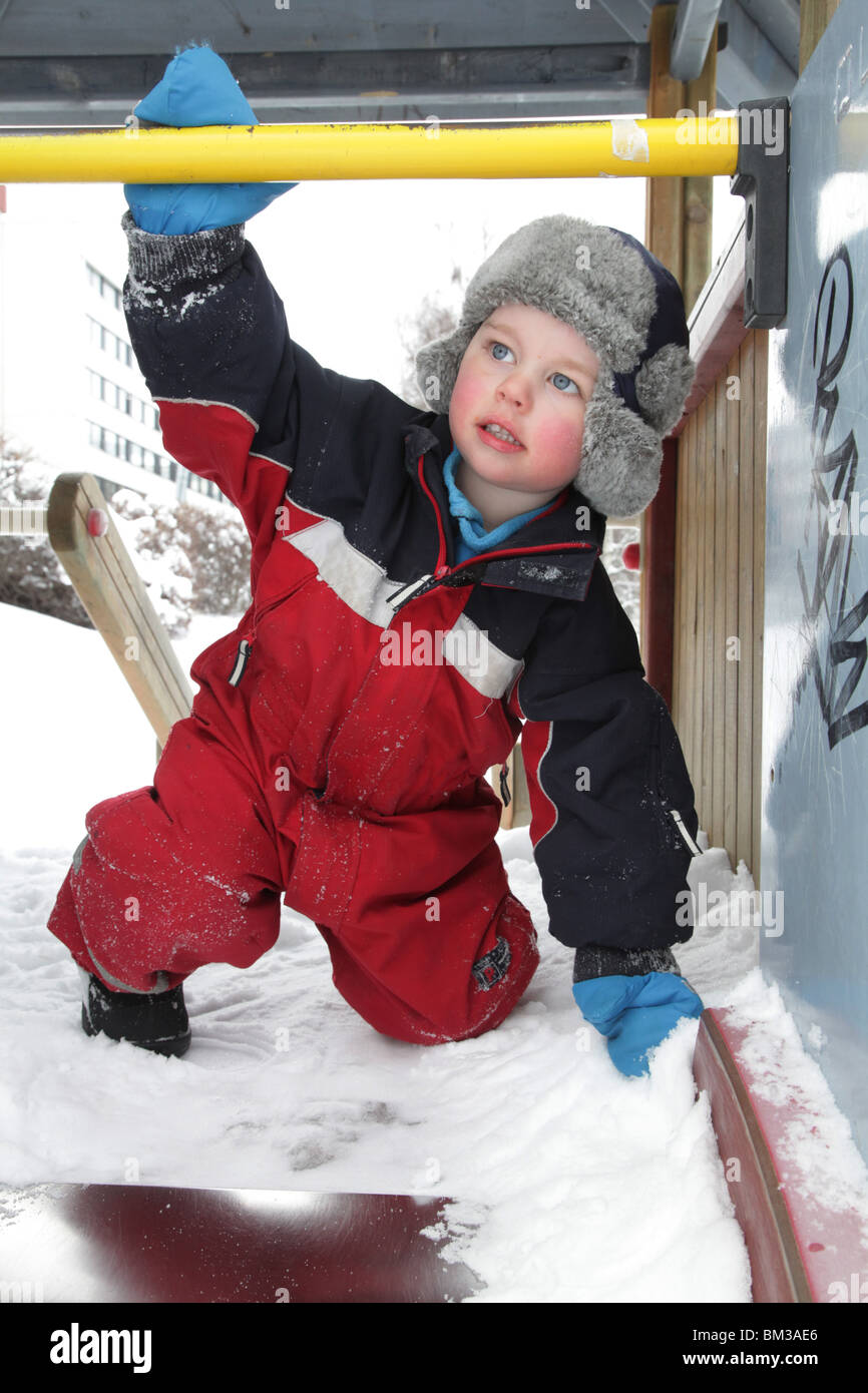 KLEINKIND BABY BOY SPIELT IM TIEFEN WINTER AUF Einer RUTSCHE: Ein zweijähriges Baby-Kind spielt auf einer Rutsche in einem Spielpark-Modell Stockfoto