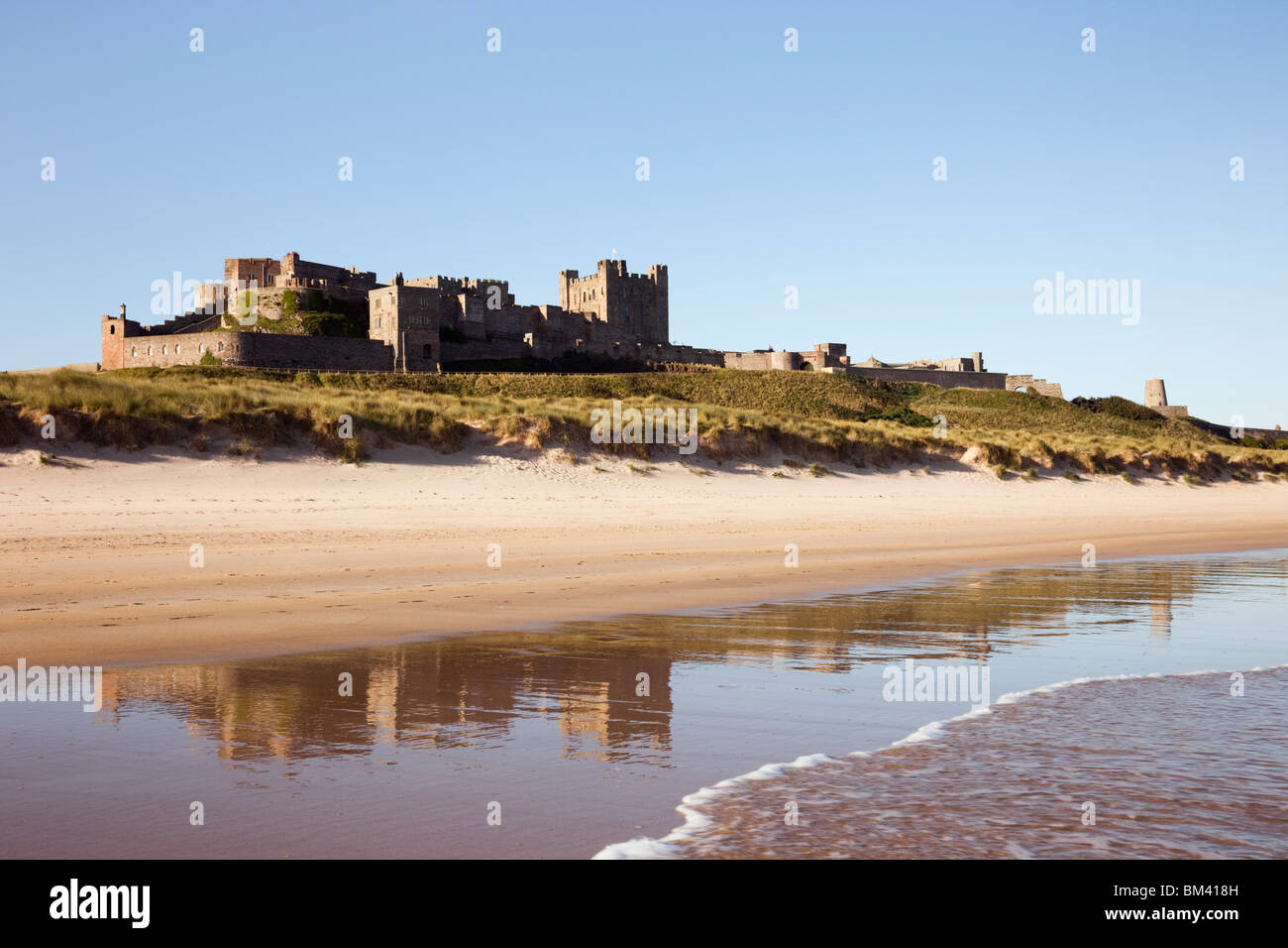 Bamburgh Castle spiegelt sich in nassem Sand am ruhigen, leeren Strand an der Küste Northumbrias wider. Bamburgh Northumberland England, Großbritannien. Stockfoto