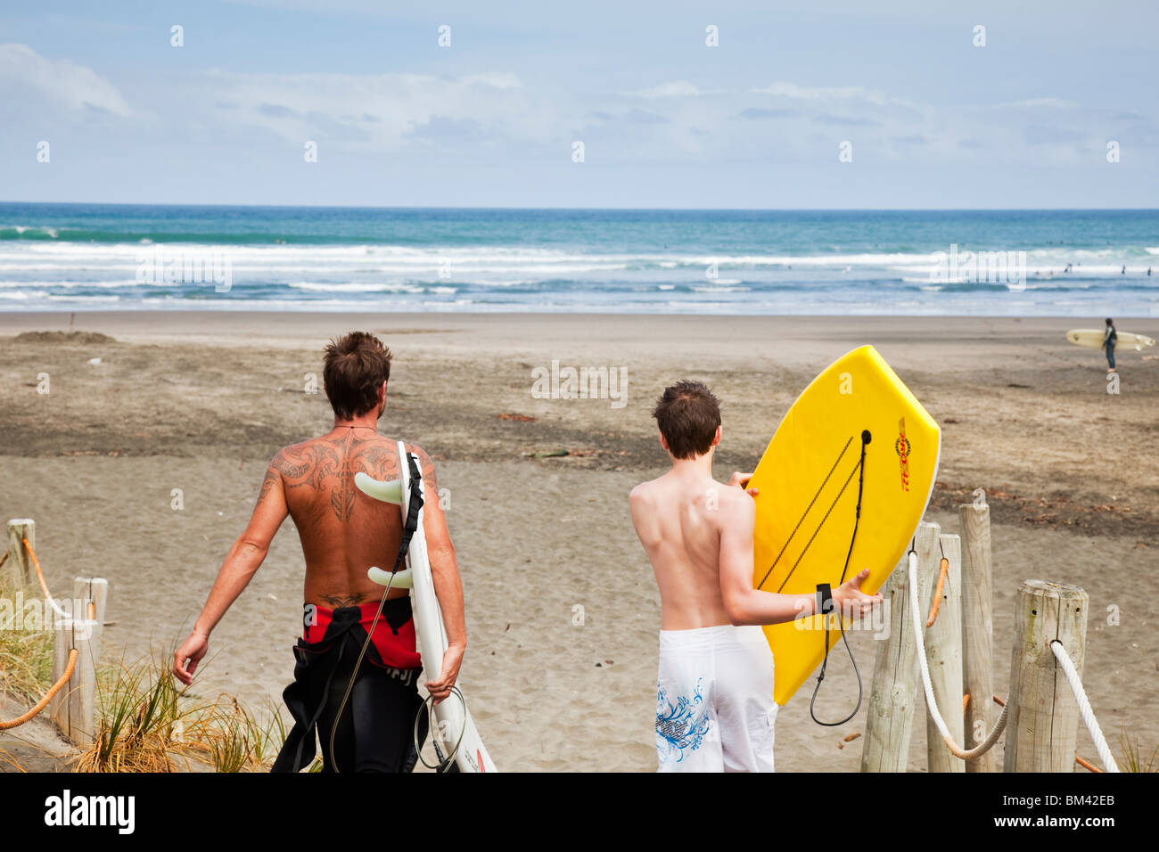 Surfer und Boogie Boarder Piha Strand hinunter wandern. Piha, Waitakere Ranges Regional Park, Auckland, Nordinsel, Neuseeland Stockfoto