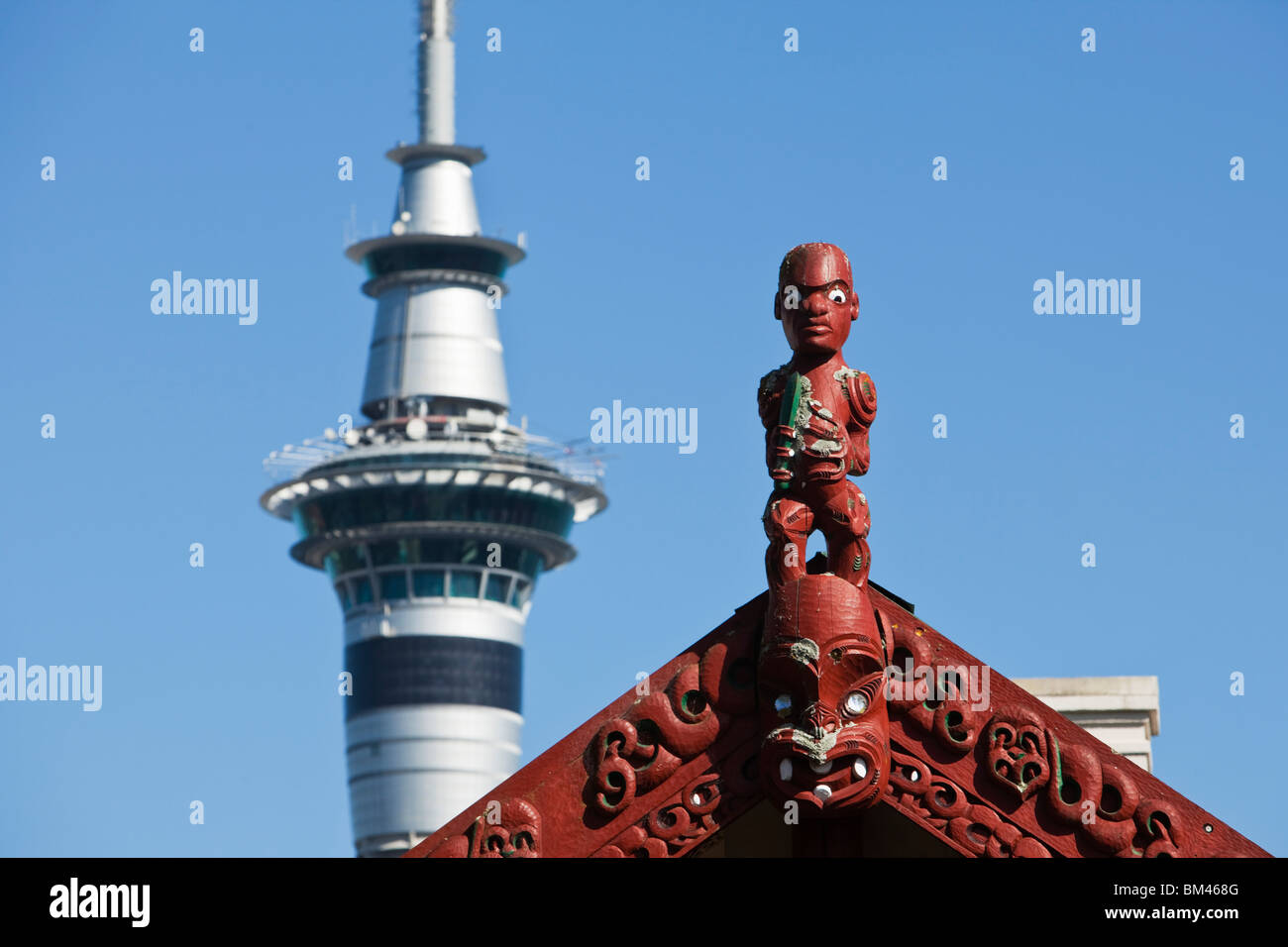 Die Maori-Schnitzereien eine Whare Runanga (Gemeindehaus) und der Sky Tower darüber hinaus. Auckland, Nordinsel, Neuseeland Stockfoto