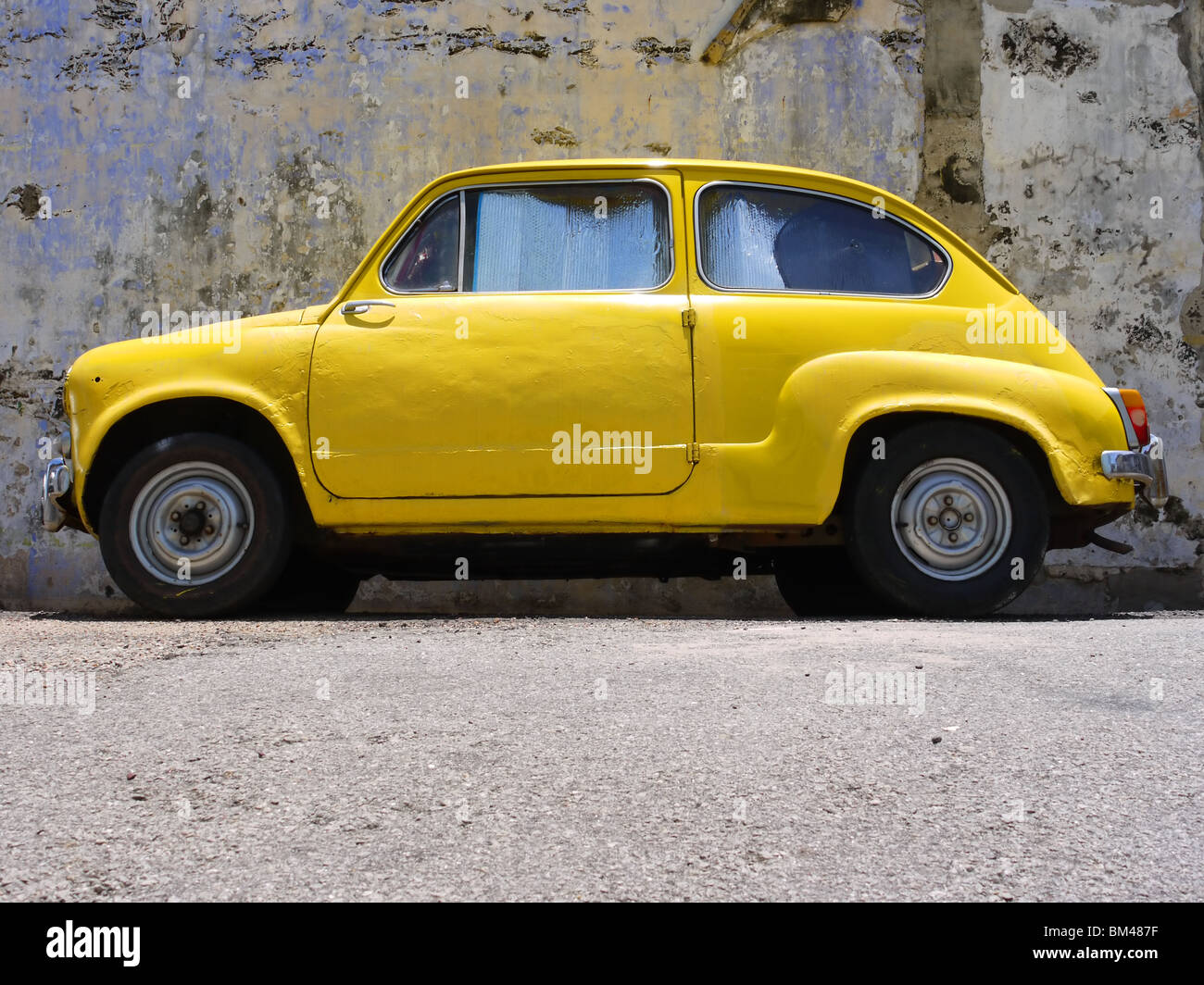 Kleine helle gelbe Oldtimer parkten in der Nähe der Wand in Malacca, Malaysia Stockfoto