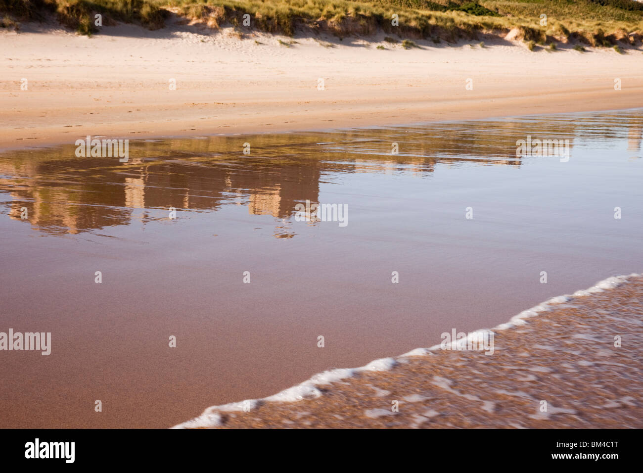 Bamburgh, Northumberland, England, Vereinigtes Königreich, Europa. Bamburgh Castle spiegelt sich im nassen Sand auf leeren Strand Vorland Stockfoto