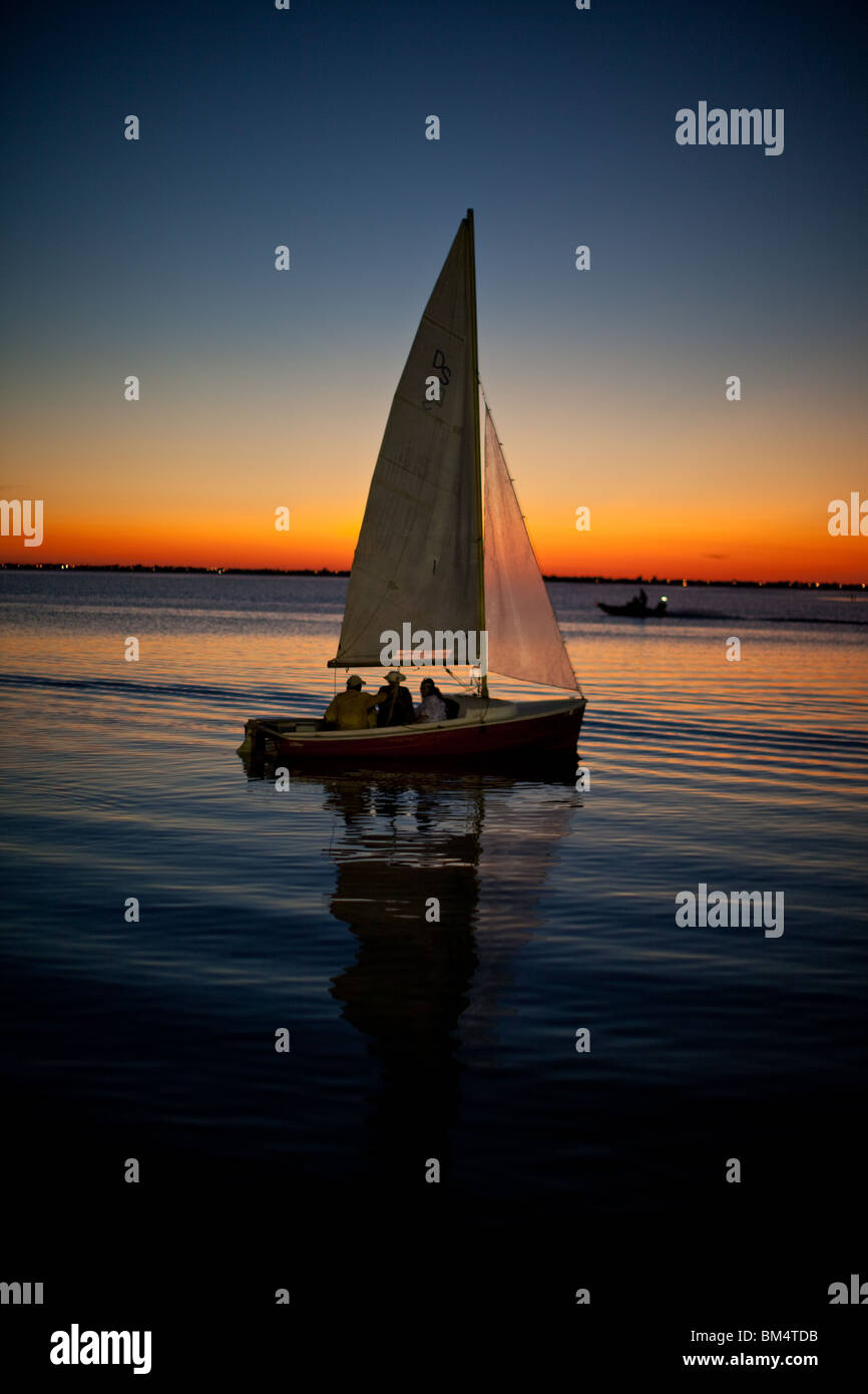 Drei Personen in einem Segelboot in Ruhe Wind beobachten den Sonnenuntergang in Corpus Christi Bay in der Nähe von Corpus Christi, Texas, USA Stockfoto