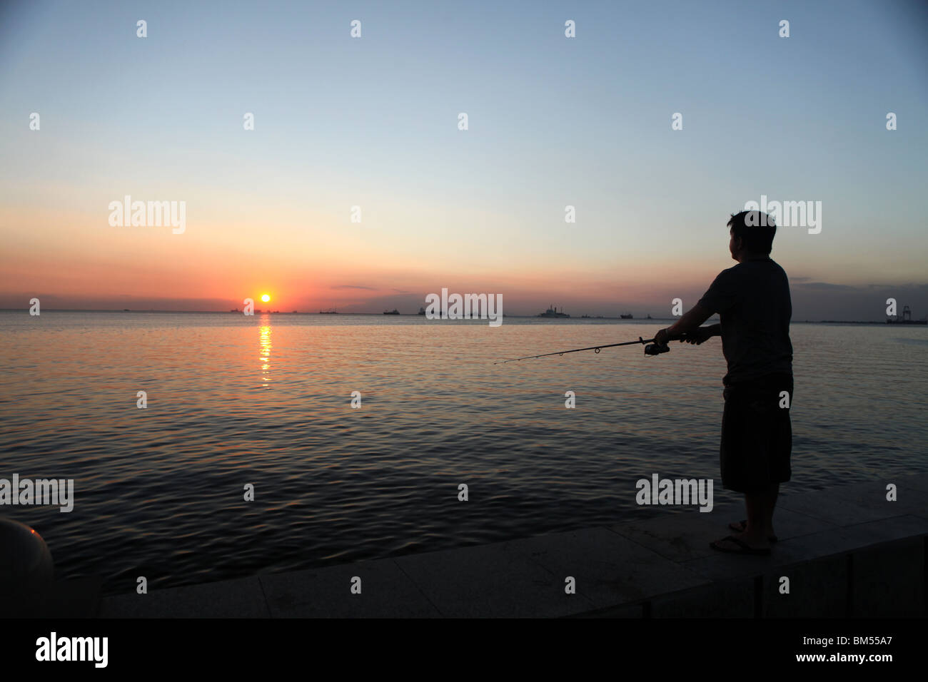 Ein Fischer wirft seine Linie in Manila Bay von Roxas Boulevard als die Sonne untergeht in der Nähe des Malat in Manila, Philippinen. Stockfoto
